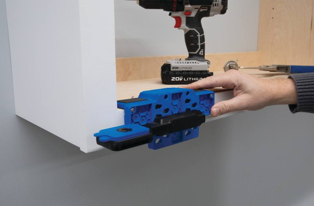 Blue cabinet door mounting jig with black grips attached to white cabinet for woodworking tool setup