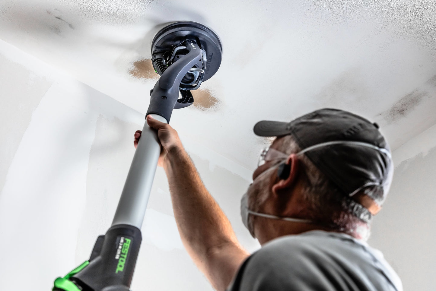 Man using a Festool drywall sander to smooth a ceiling in a home improvement power tools setting