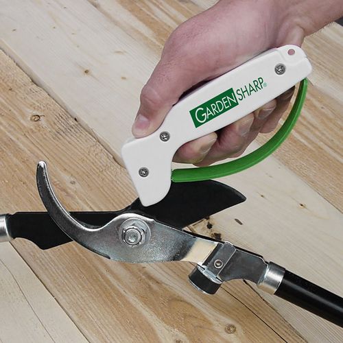 Handheld white and green tool sharpener used on a pruning shear blade for gardening and woodworking tasks