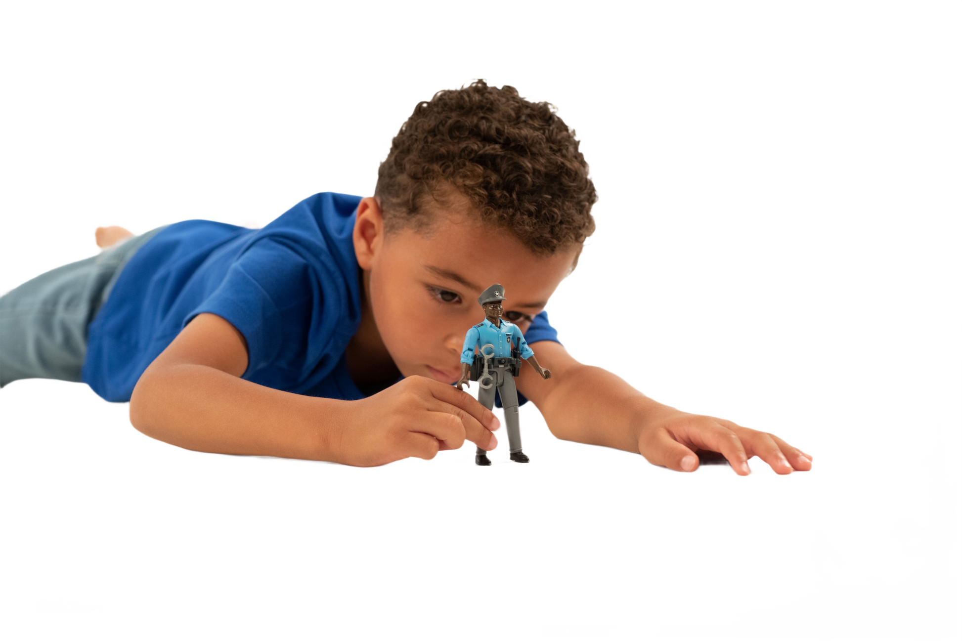 Young boy in blue shirt lying down playing with dark-skinned policeman toy figure wearing blue uniform and cap