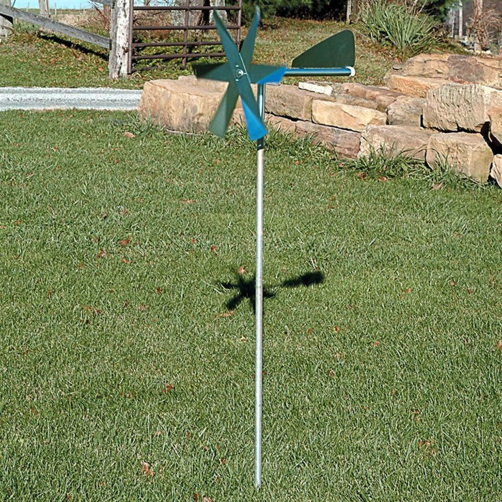Metal lawn windmill with spinning blades and tail vane mounted on pole for mole pest deterrence in garden setting