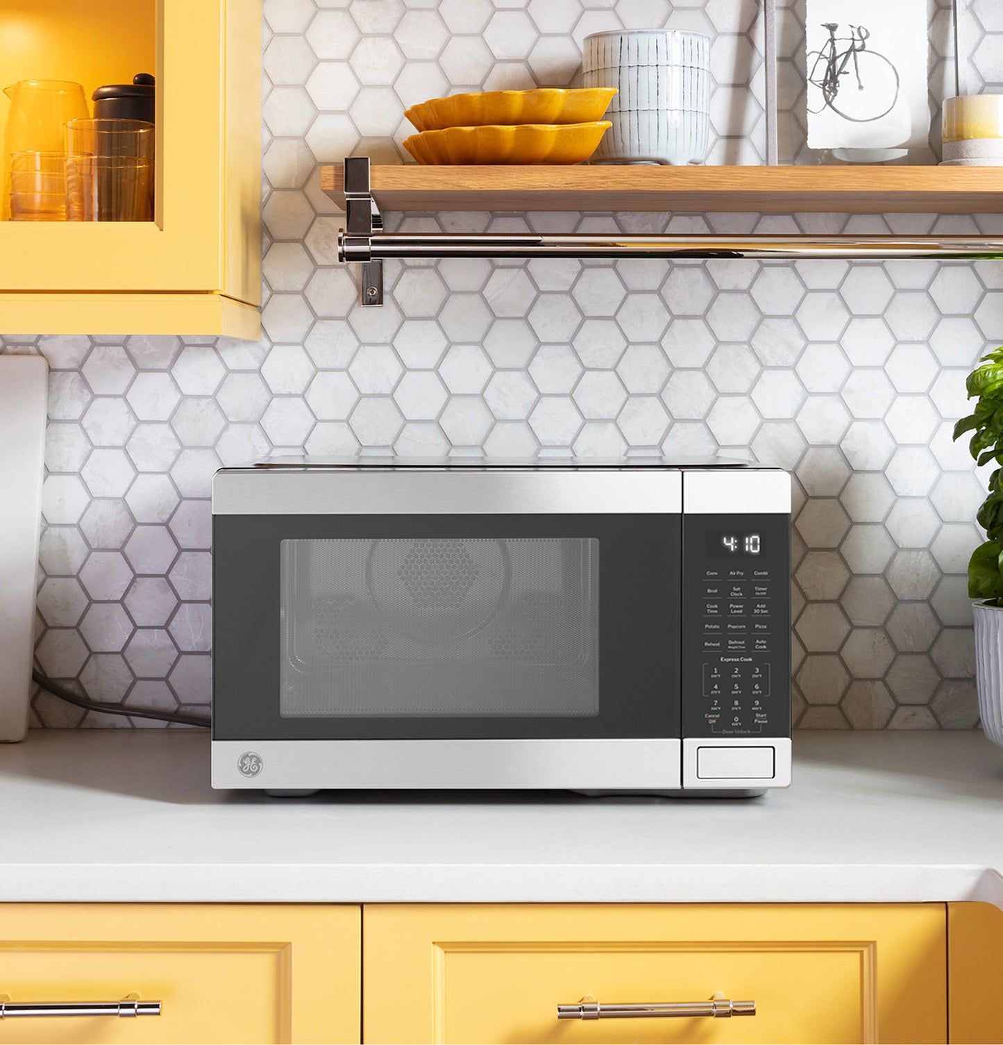 Compact stainless steel microwave oven with digital control panel on white kitchen countertop with yellow cabinetry