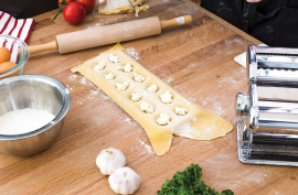 Aluminum jumbo ravioli mold making 10 square stuffed pasta on wooden countertop with rolling pin and pasta machine nearby