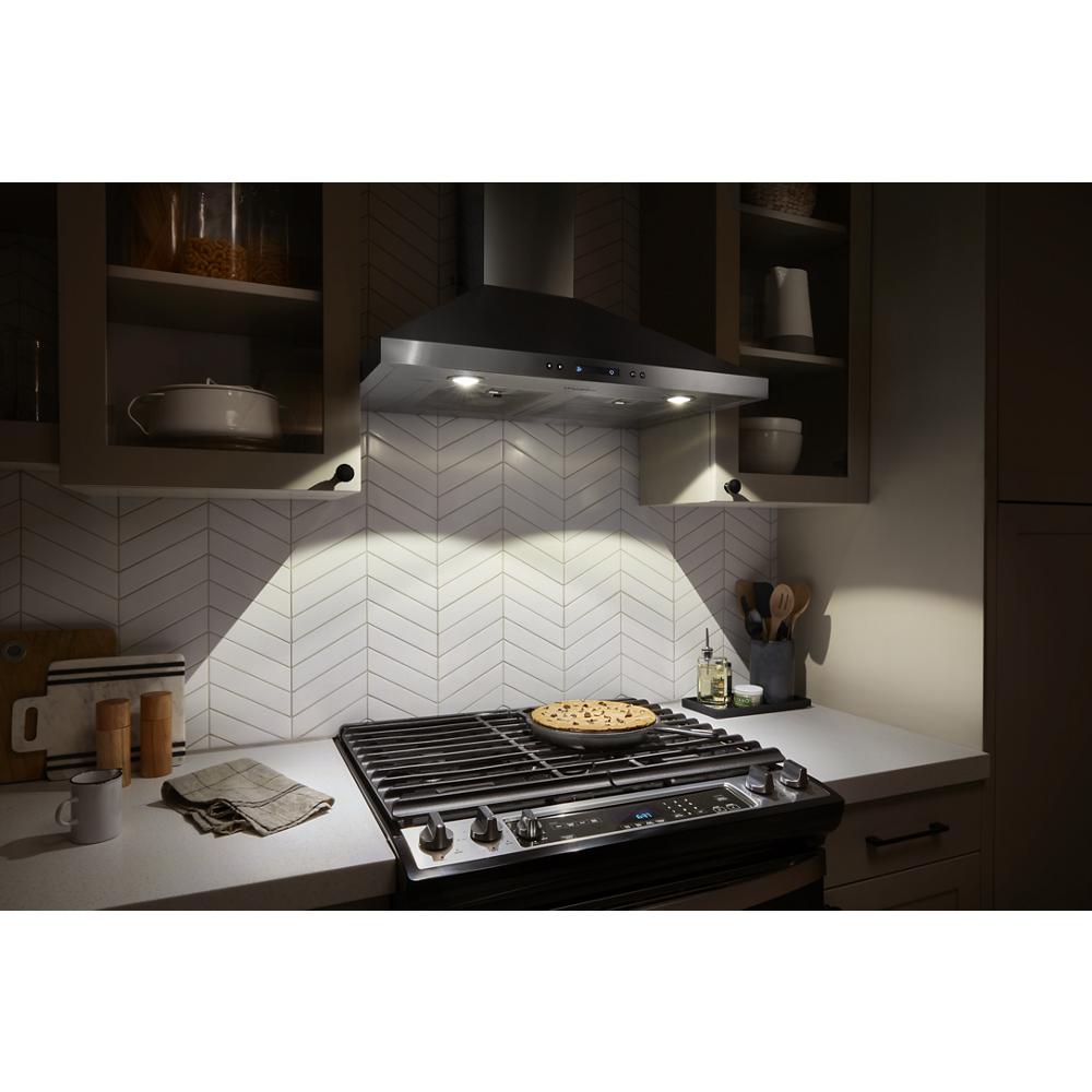 Sleek stainless steel chimney range hood with LED lights above a gas stove in a modern kitchen setting