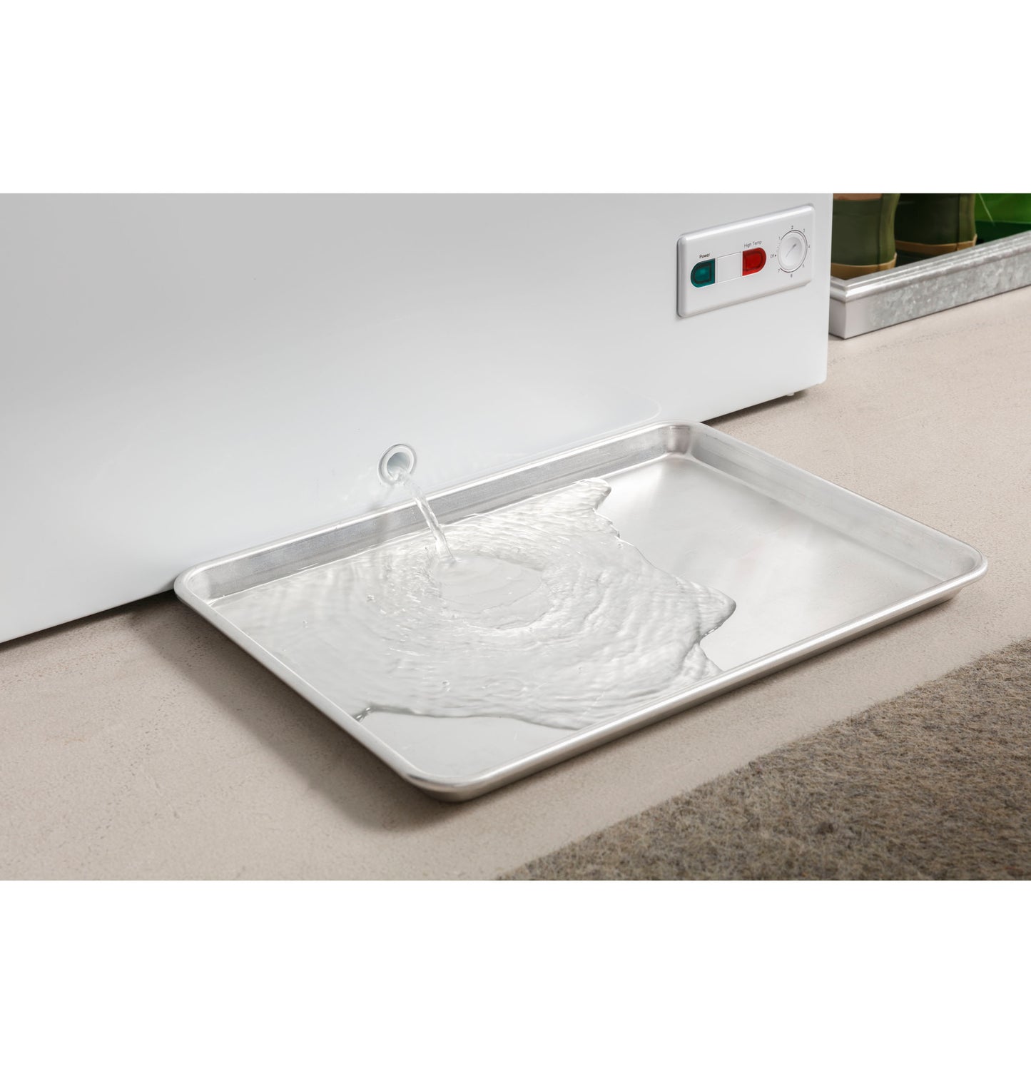 Manual defrost chest freezer with water draining into a metal tray on the floor near control panel buttons