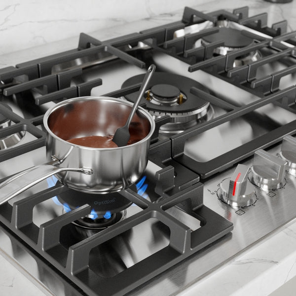 Stainless steel gas cooktop with blue flame burner heating a pot of chocolate sauce in modern kitchen setting