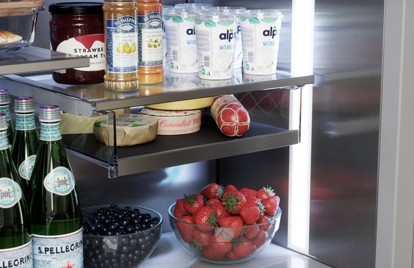 Inside stainless steel fridge door with glass shelves holding yogurt, jam, beverages, fresh strawberries, and blackberries