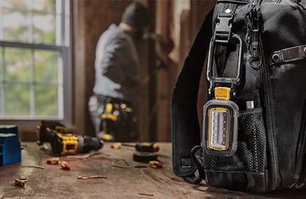 Rechargeable LED work light attached to black tool bag with person working on home improvement project in background
