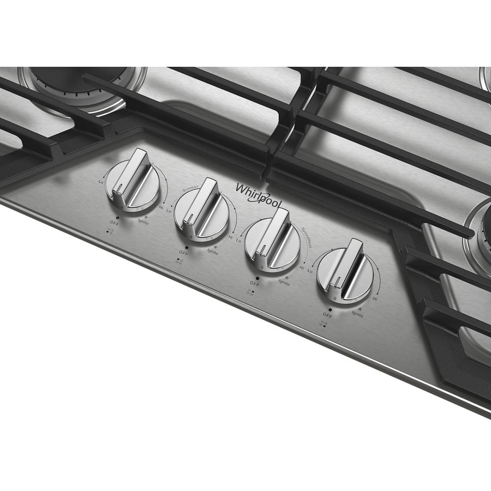 Close-up of stainless steel cooktop control panel with four knobs and cast-iron grates from kitchen appliances collection
