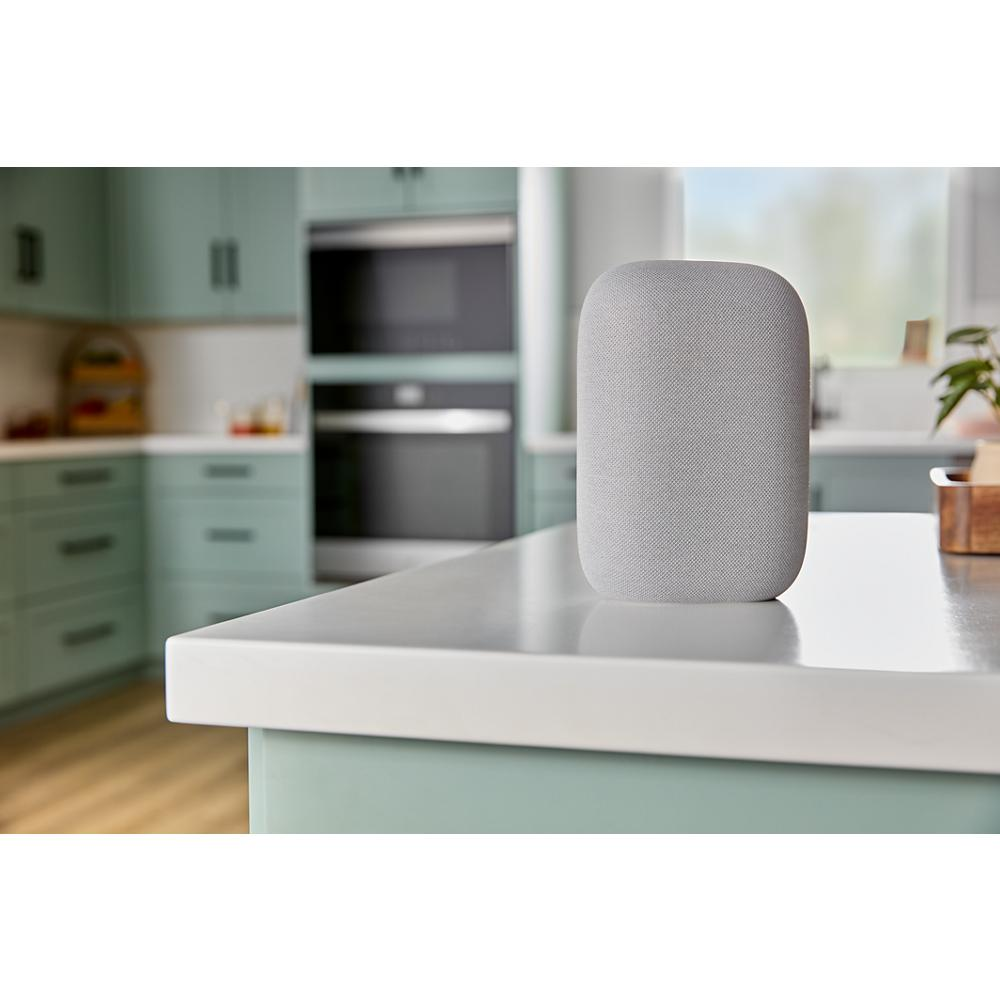 Smart speaker with fabric cover placed on kitchen countertop in modern home with built-in appliances visible in background
