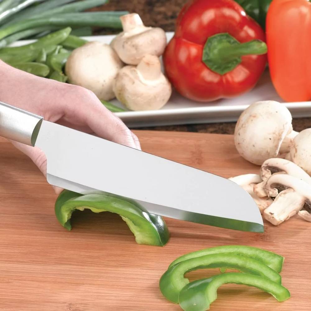Hand using stainless steel cooks knife slicing green bell pepper on wooden cutting board with mushrooms nearby