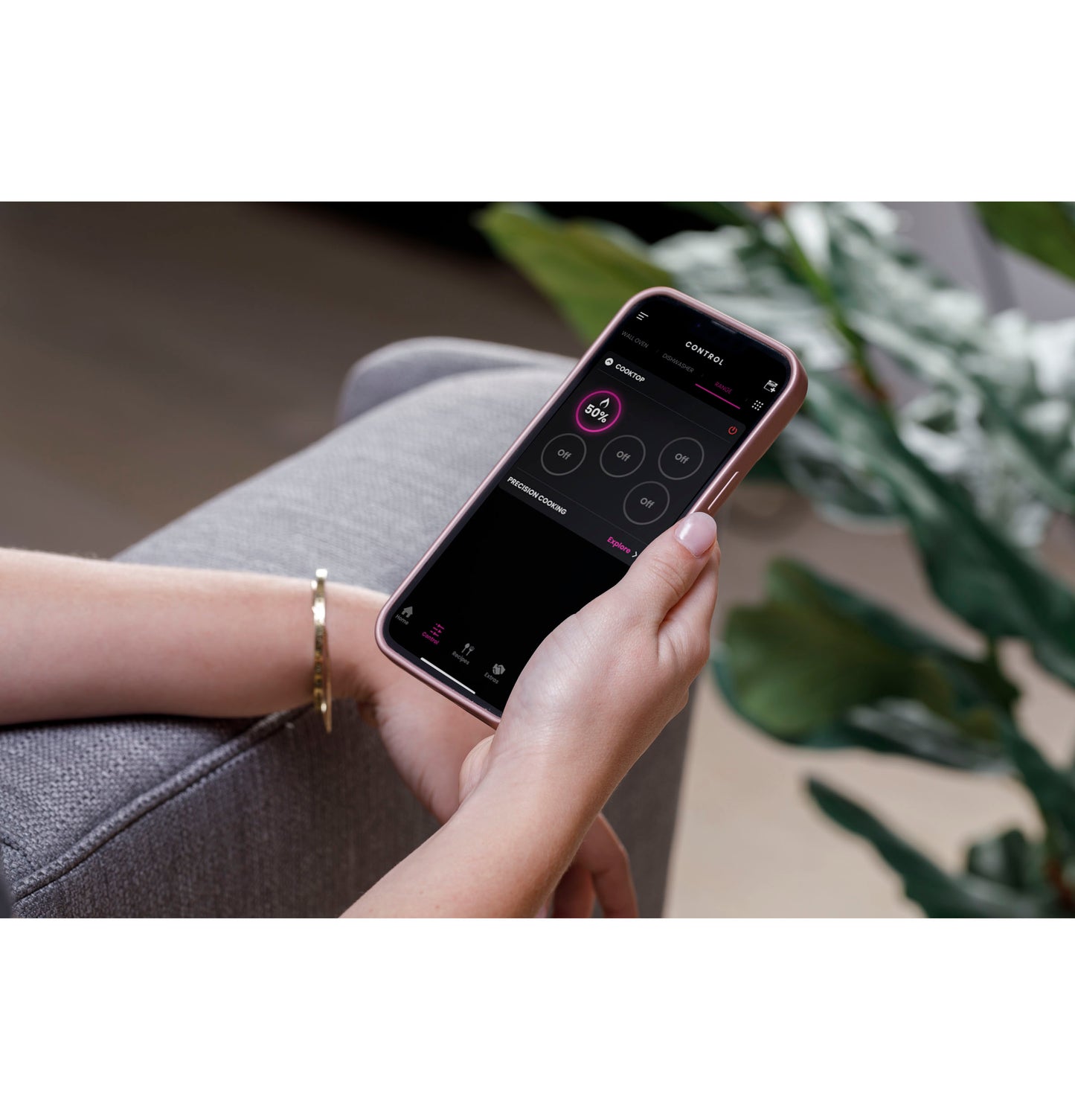 Person holding smartphone with app open showing kitchen appliance controls in home improvement setting
