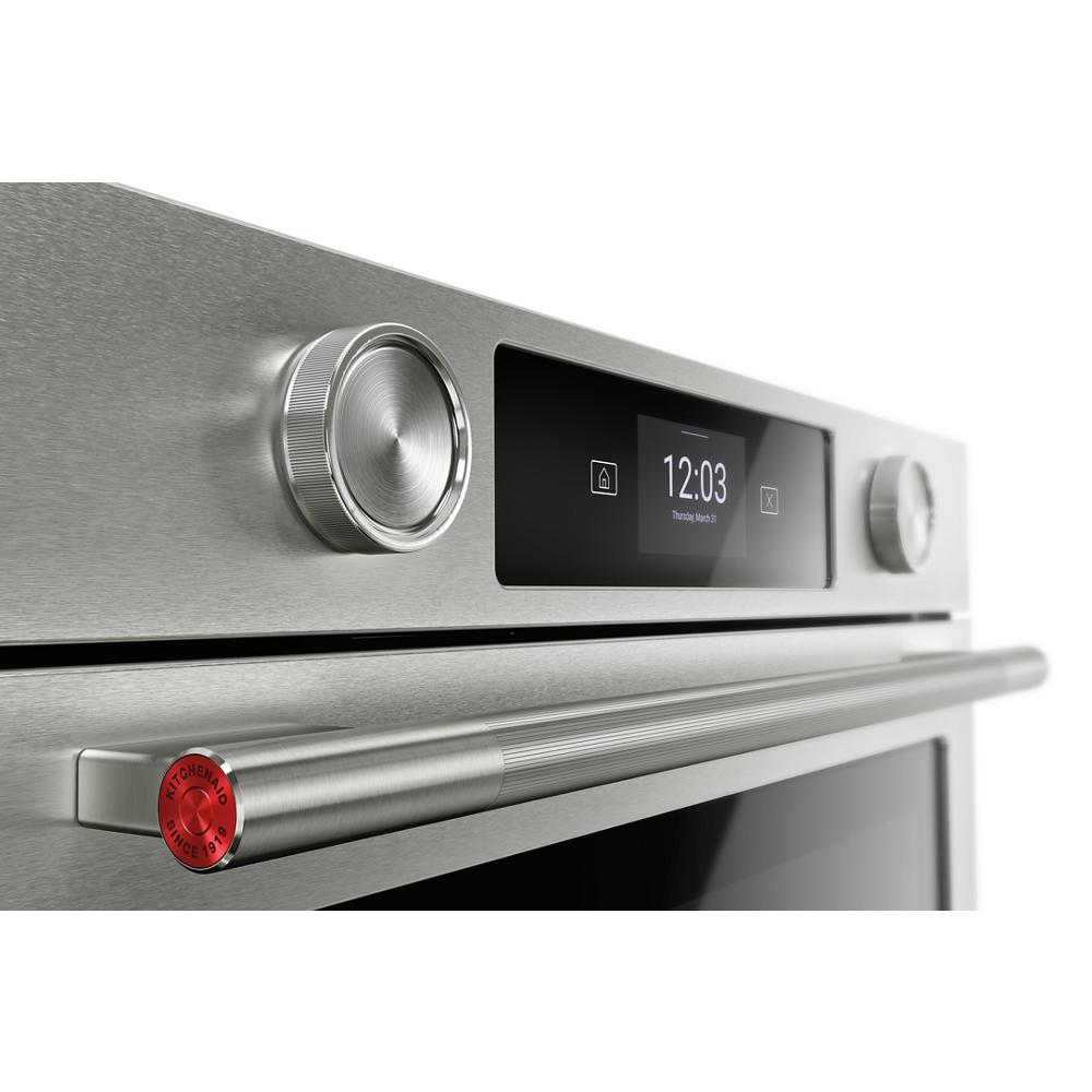Close-up of a stainless steel smart electric wall oven control panel with LED display and textured knobs in modern kitchen setting