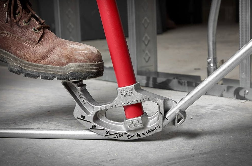 Aluminum conduit bender with red handle bending metal EMT conduit on concrete surface in a construction setting