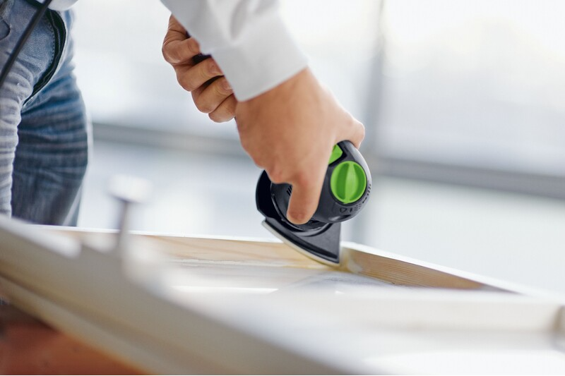 Person holding a compact black and green multi-mode sander smoothing a white wooden frame for home improvement tasks