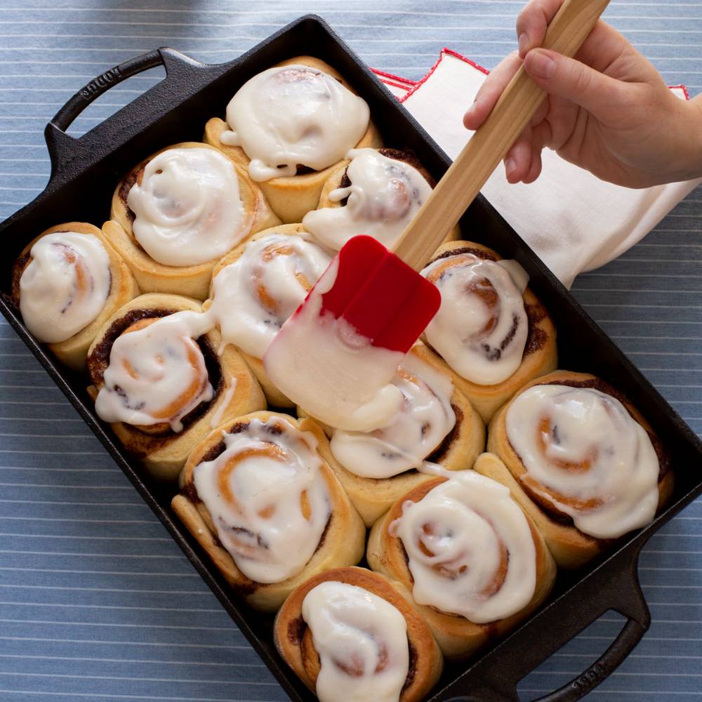 Rectangular cast iron pan with freshly baked cinnamon rolls being iced for Kitchenware and Lodge Cast Iron collections