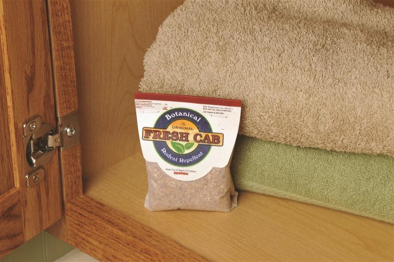 Small pouch of botanical rodent repellent granules placed inside wooden cabinet near folded towels