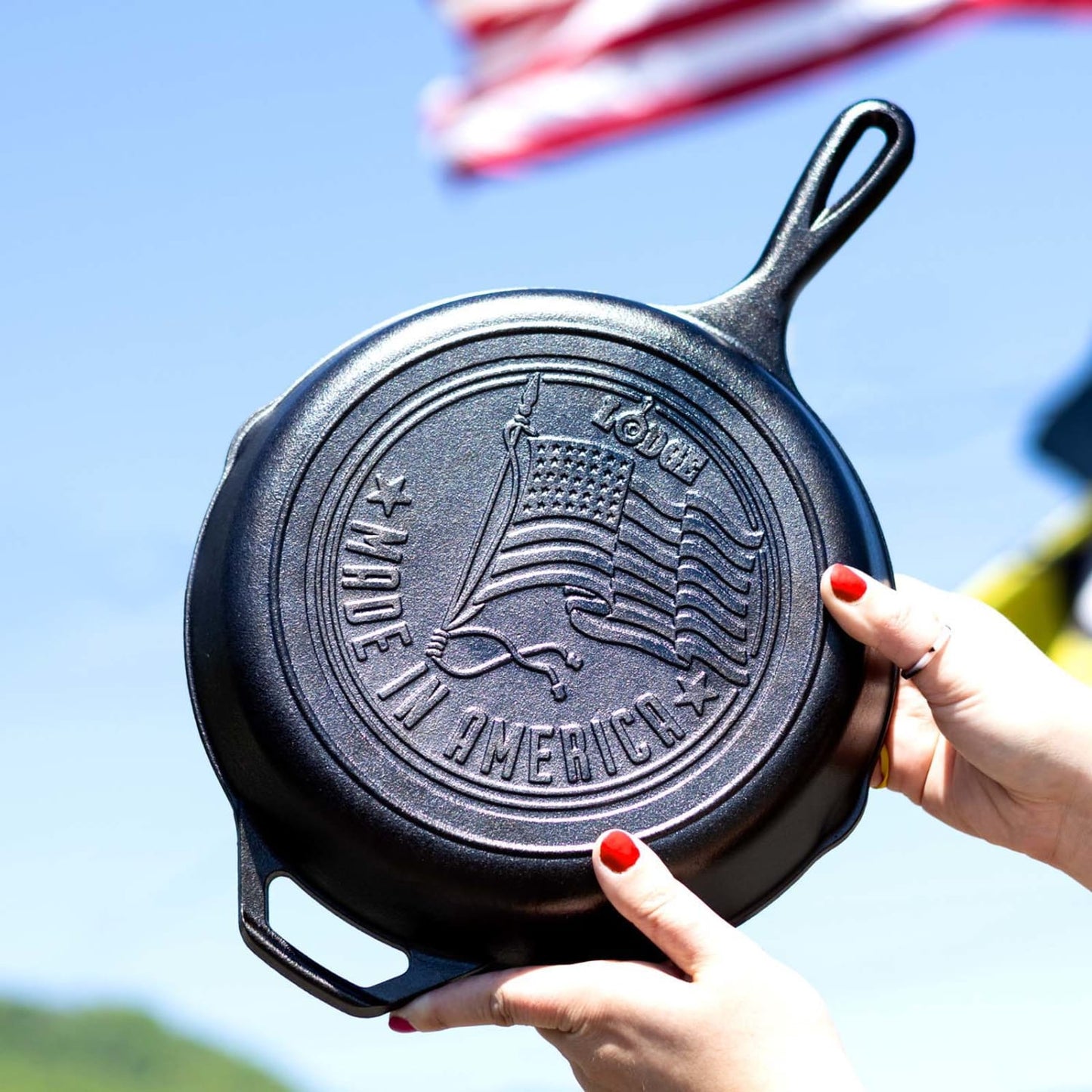 Hands holding seasoned cast iron skillet with embossed American flag and made in America text outdoors kitchenware product