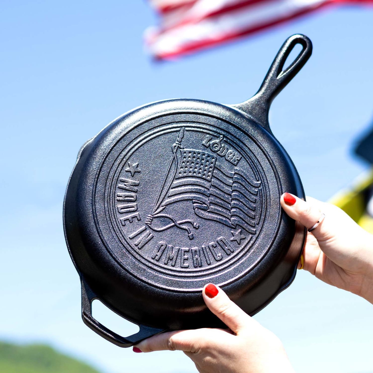 Hands holding seasoned cast iron skillet with embossed American flag and made in America text outdoors kitchenware product