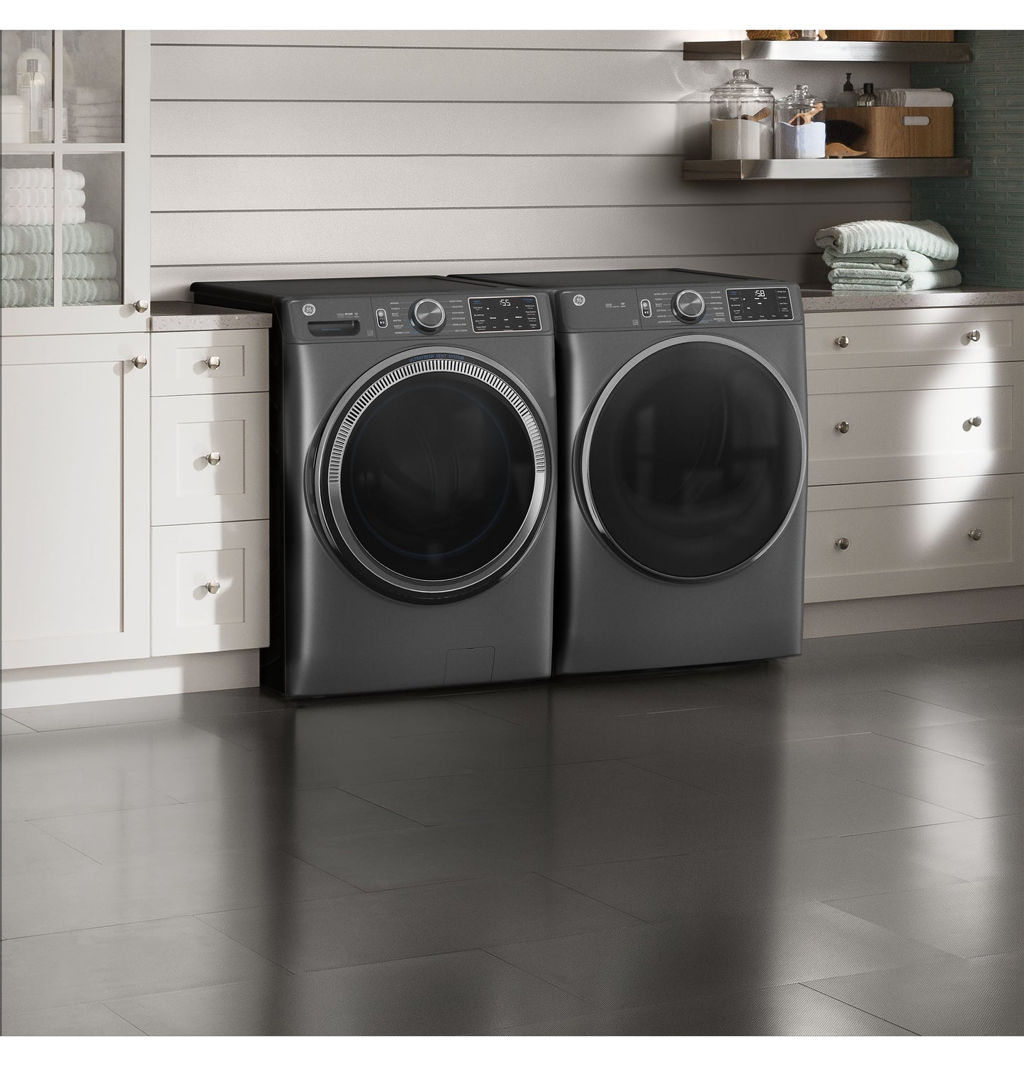 Pair of dark gray front load washer and electric dryer with digital controls in modern laundry room setting