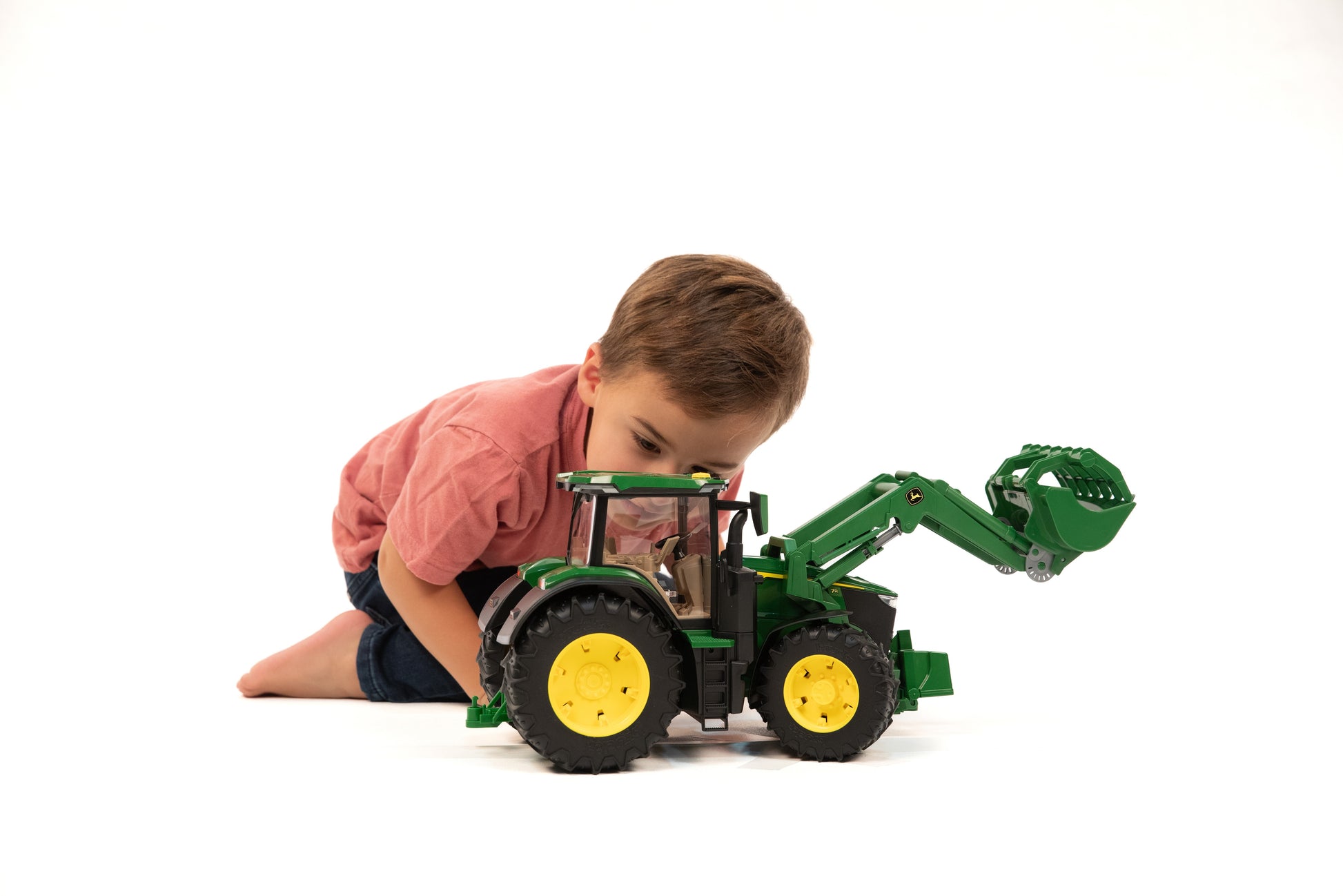 Young boy engaged with green Bruder John Deere 7R 350 toy tractor featuring movable front loader for home improvement play