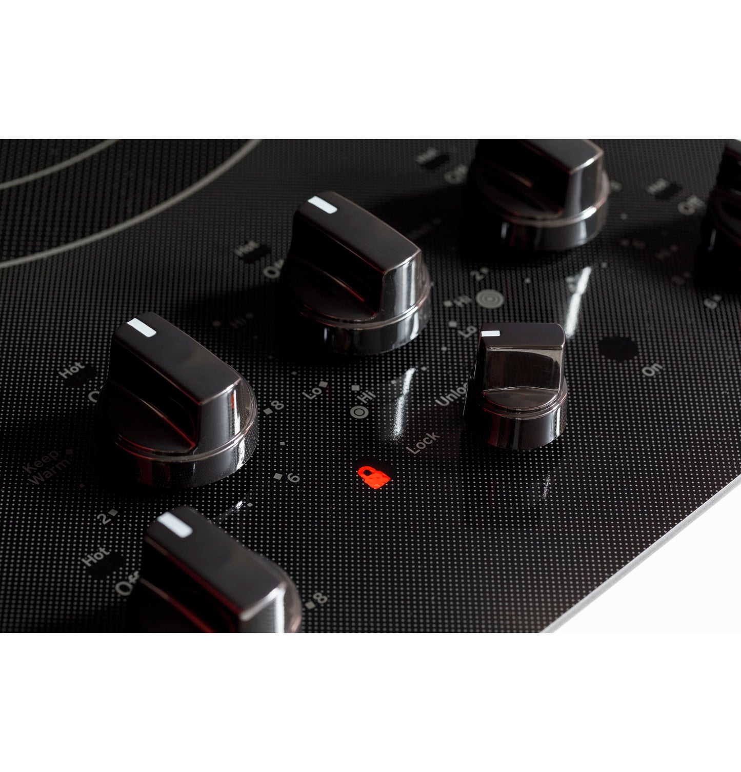 Close-up of black knob controls with safety lock indicator on a GE 36-inch built-in electric cooktop surface