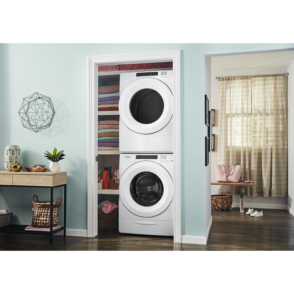 Stacked white front load washer and heat pump dryer set in laundry nook with shelving and folded towels nearby