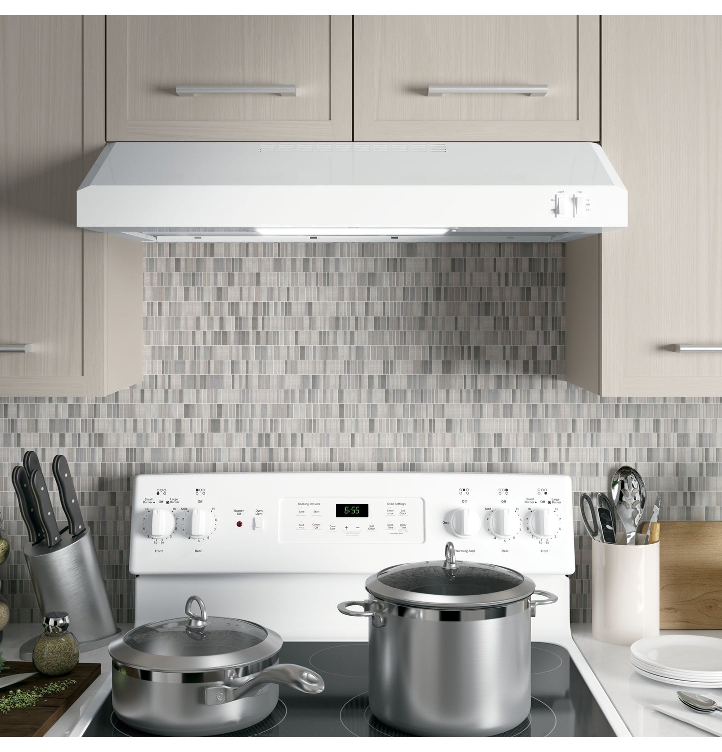 Under-cabinet white range hood above cooktop with gray mosaic tile backsplash in modern kitchen setting