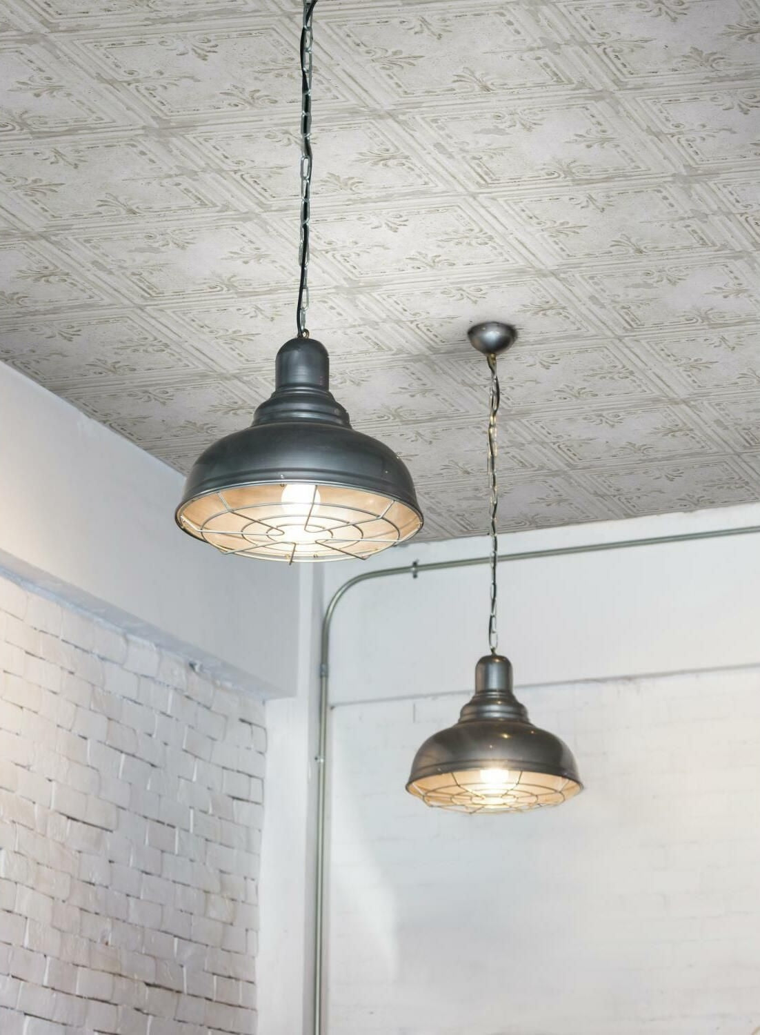 Industrial style hanging pendant lights with metal shades illuminating a room with embossed tin tile wallpaper ceiling