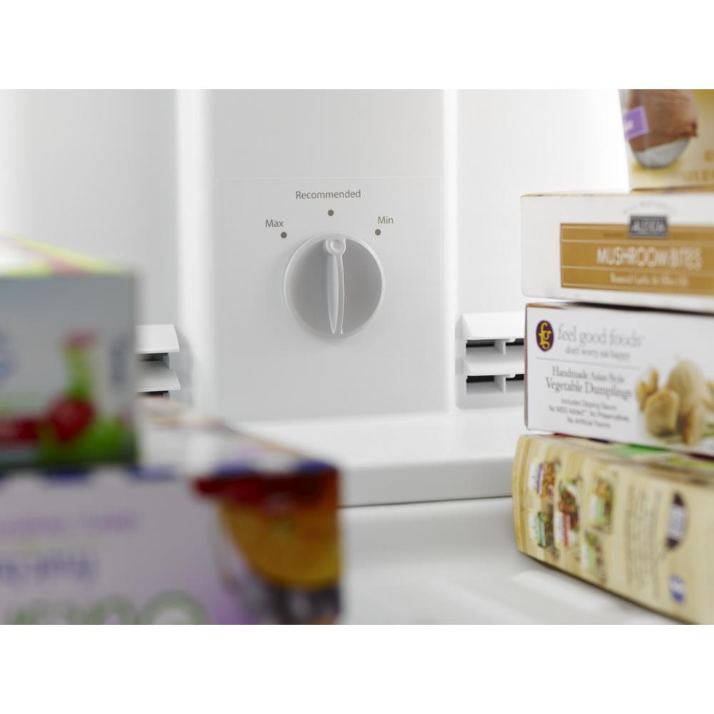 Close-up of white top freezer refrigerator temperature control dial with packaged food boxes nearby in kitchen appliances setting