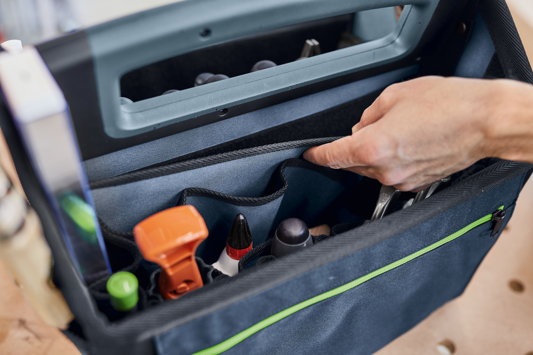 Close-up of a hand organizing tools inside a durable black and green tool bag for workshop and jobsite storage