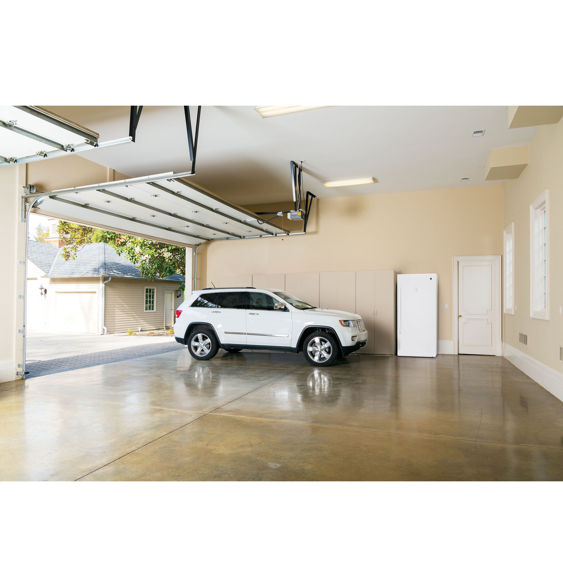 White frost-free upright freezer positioned against wall in spacious home garage with white SUV nearby