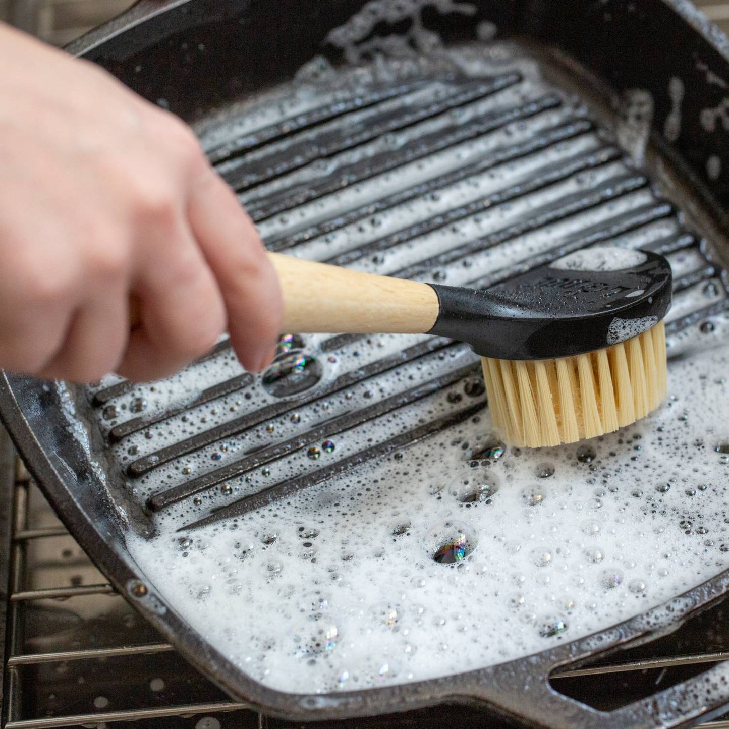 Cleaning a cast iron grill pan with a wooden handled stiff nylon scrub brush in kitchenware and tools collections under $50