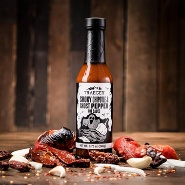 Traeger smoky chipotle and ghost pepper hot sauce bottle surrounded by dried peppers and garlic in Grilling Sauces & Spices collection