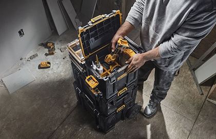 Person organizing cordless power drills and accessories in a sturdy yellow and black tool chest for jobsite storage