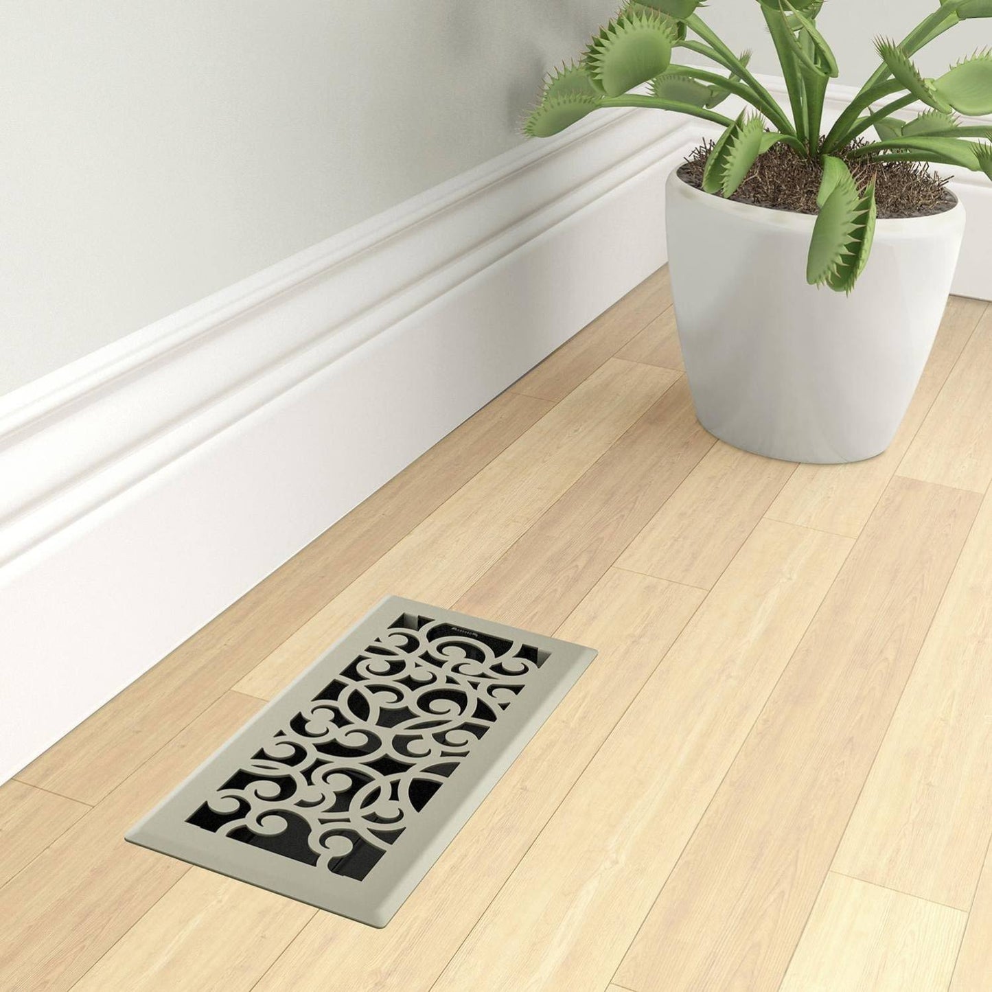 Satin nickel floor register with ornate swirling pattern on light hardwood floor near white baseboard and plant pot in Plumbing collection