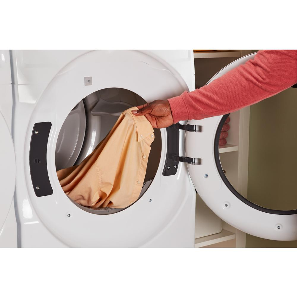 Hand placing tan shirt into open white front load electric dryer in laundry room for home improvement use