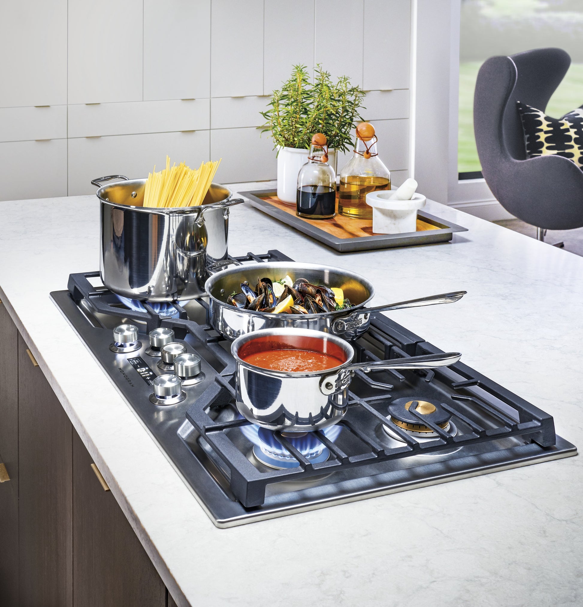 Monogram 36-inch deep-recessed gas cooktop with stainless steel cookware simmering sauce and boiling pasta in modern kitchen
