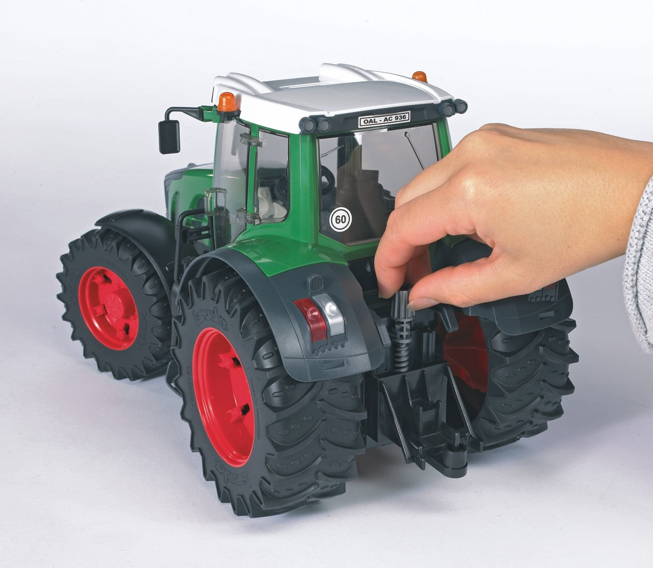 Hand adjusting the rear hitch mechanism of a green Bruder Fendt 936 Vario Tractor toy with red wheels