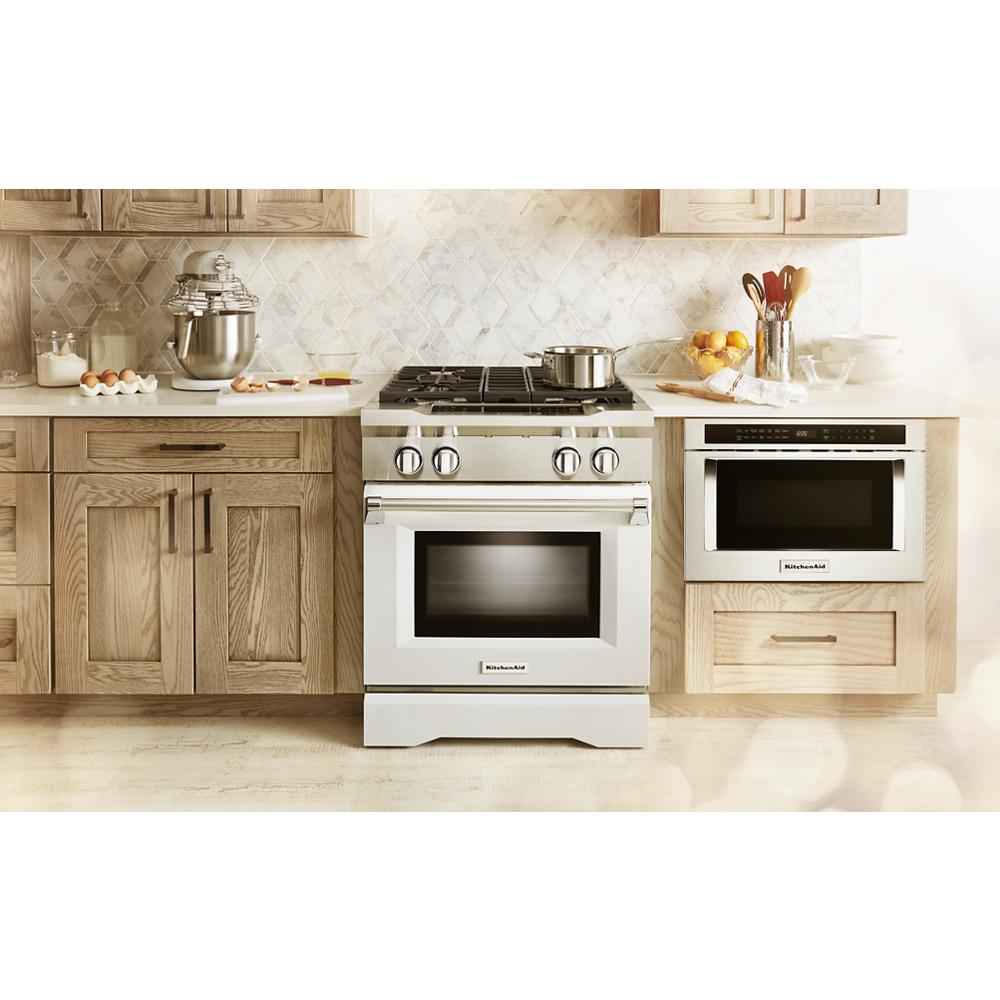 Built-in under-counter microwave drawer installed in wood cabinetry next to stainless steel gas range in kitchen setting