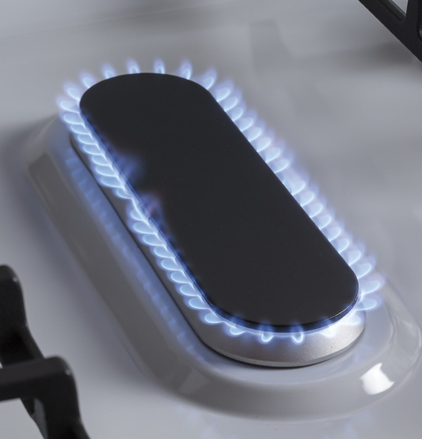 Close-up of gas burner with blue flame on white cooktop in kitchen appliances and gas ranges collection