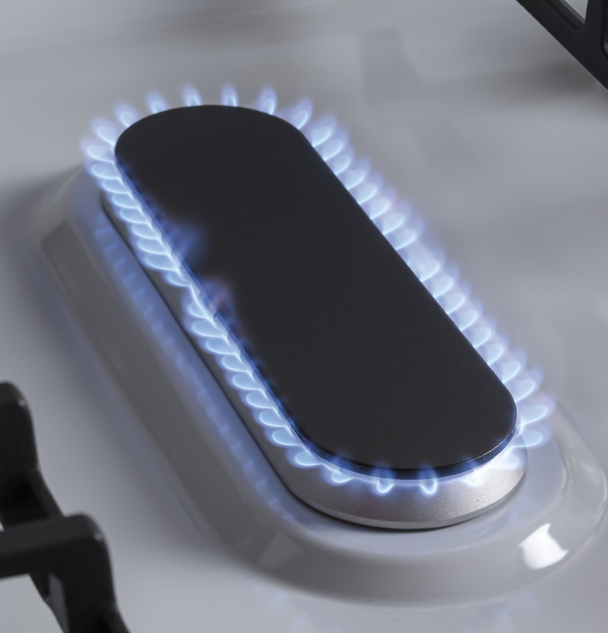 Close-up of gas burner with blue flame on white cooktop in kitchen appliances and gas ranges collection