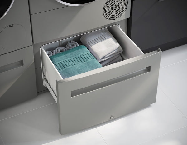 Open drawer with neatly folded towels stored below compact front load washer in modern laundry setting