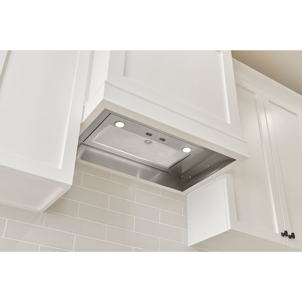 Undermount stainless steel range hood insert with LED lights installed under white kitchen cabinets in a modern kitchen