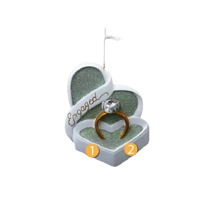 Heart-shaped glittery Christmas ornament featuring a gold engagement ring with a large clear gem and "Engaged" script
