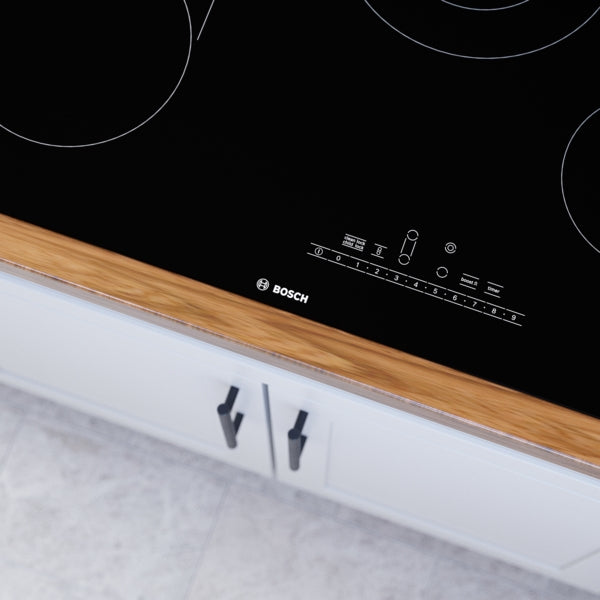 Black glass electric cooktop with touch slider controls and four cooking zones on wood-trimmed countertop surface