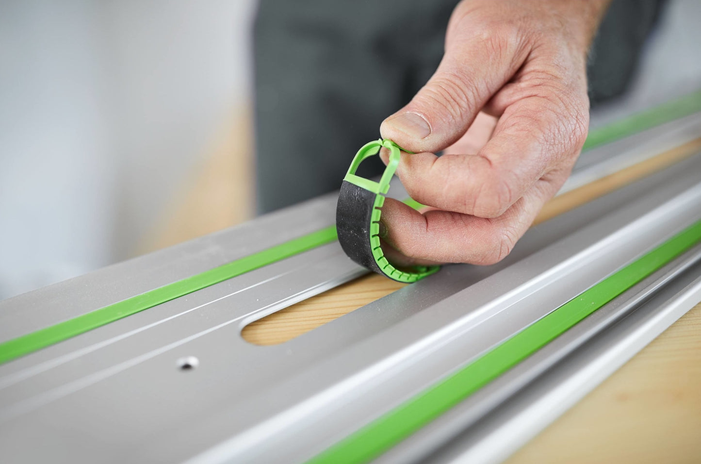 Hand placing black and green non-slip strip onto aluminum guide rail for woodworking tool accessory use