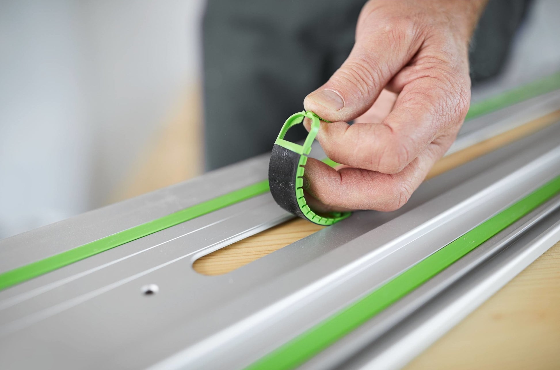 Hand placing black and green non-slip strip onto aluminum guide rail for woodworking tool accessory use