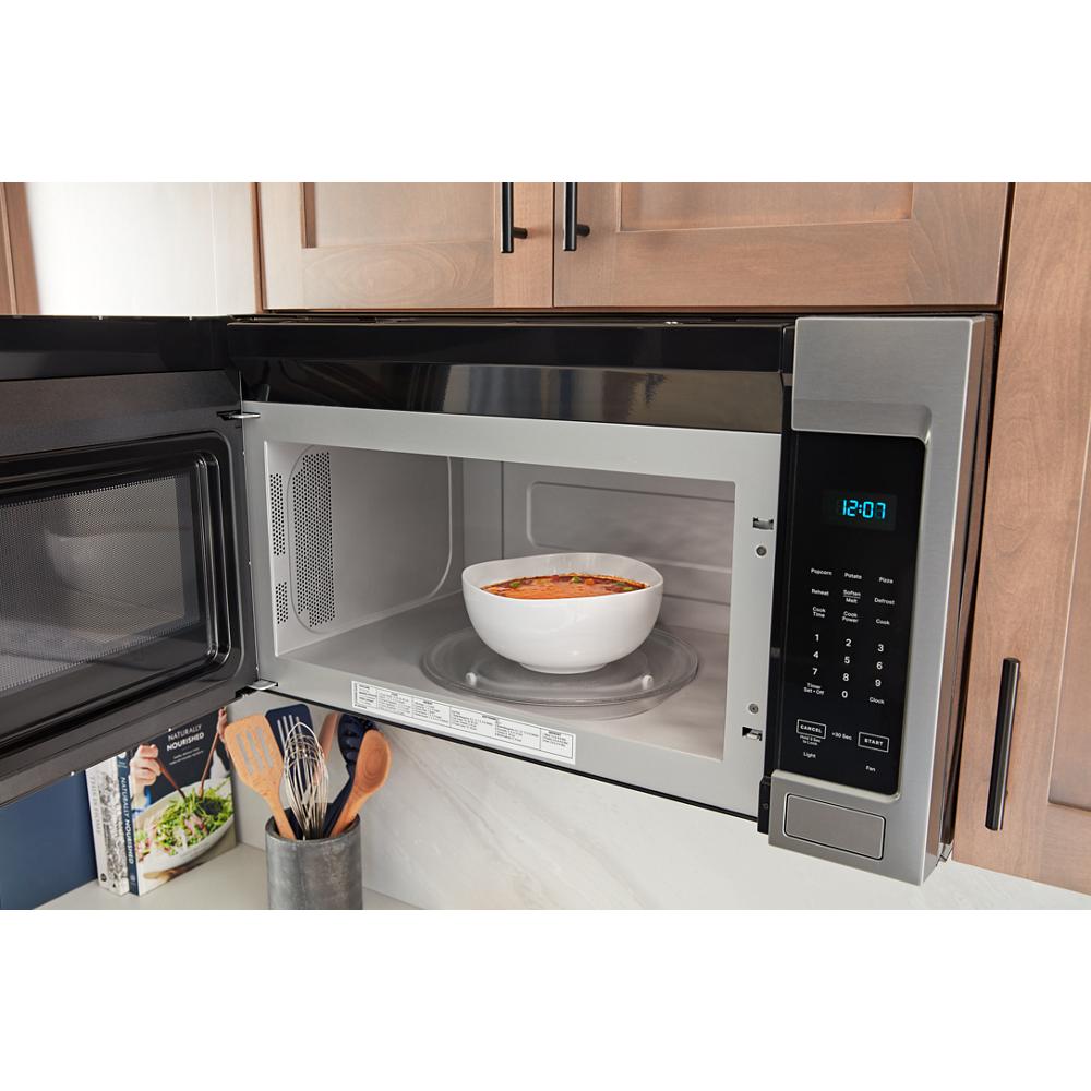 Stainless steel microwave with open door showing white bowl inside on turntable in kitchen setting