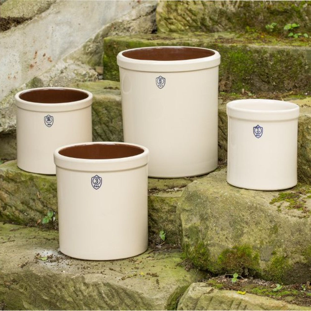 Set of cream-colored stoneware crocks with blue shield emblems and glossy brown interiors for kitchen or storage use